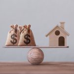 US dollar hessian bags with house paper model on a wood balance scale. Home loan, reverse mortgage concept, Depicts a homeowner or a borrower turns properties into cash